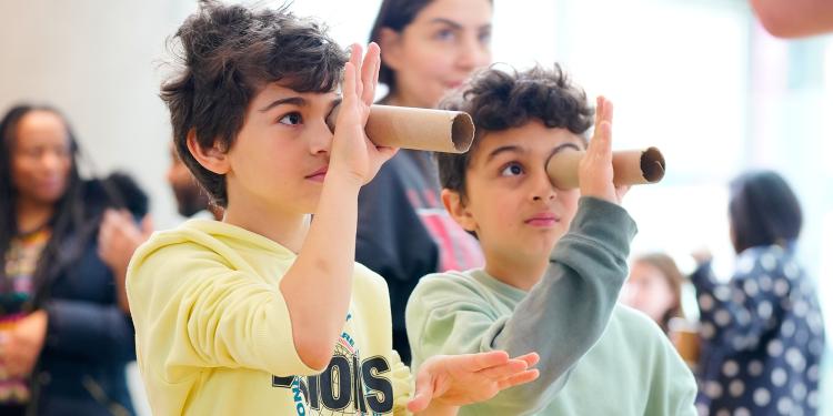 Two children look through cardboard tubes as they do a science experiment