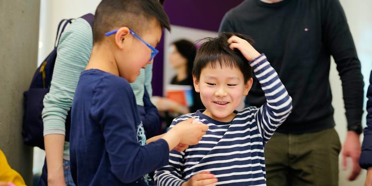 Two children look at something, one is scratching his head and smiling in delight