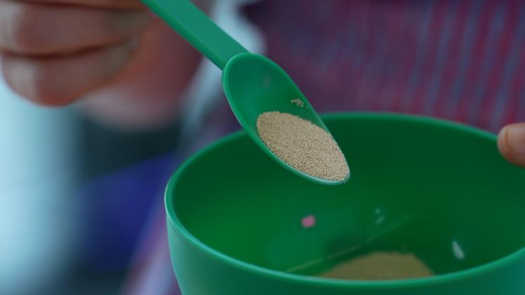 A spoonful of baker's yeast held over a green bowl