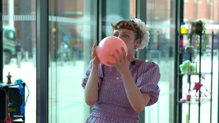 A woman is trying hard to blow up a balloon with her mouth, and is clutching it with two hands