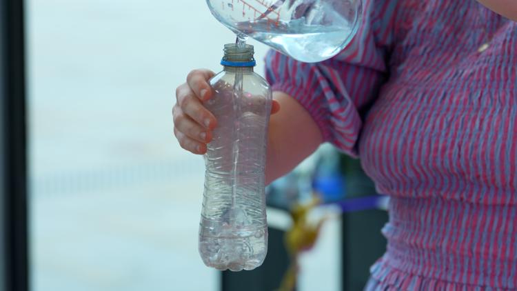 A woman holds a clear plastic bottle in one hand and pours water into it with the other hand