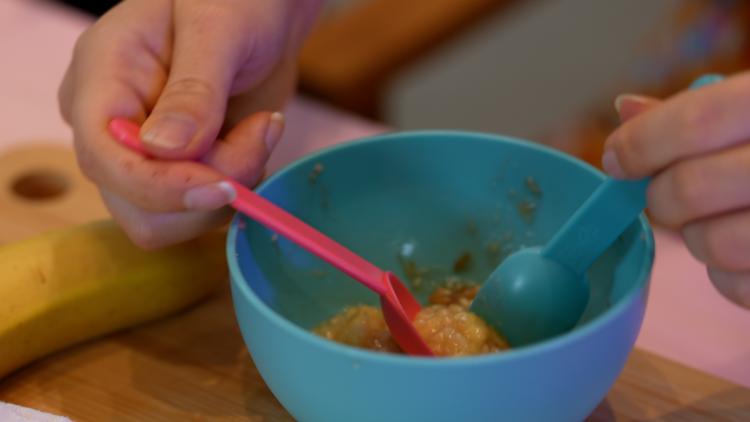 A hand using a fork to mash up banana in a bowl