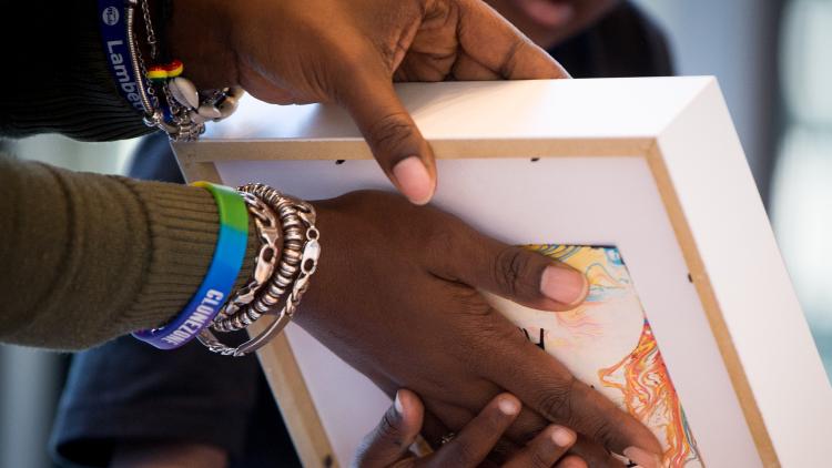 A child and adult's hands holding a piece of paper and some art in a frame.