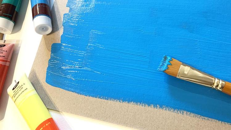 A piece of paper covered in blue paint with a paintbrush nearby.