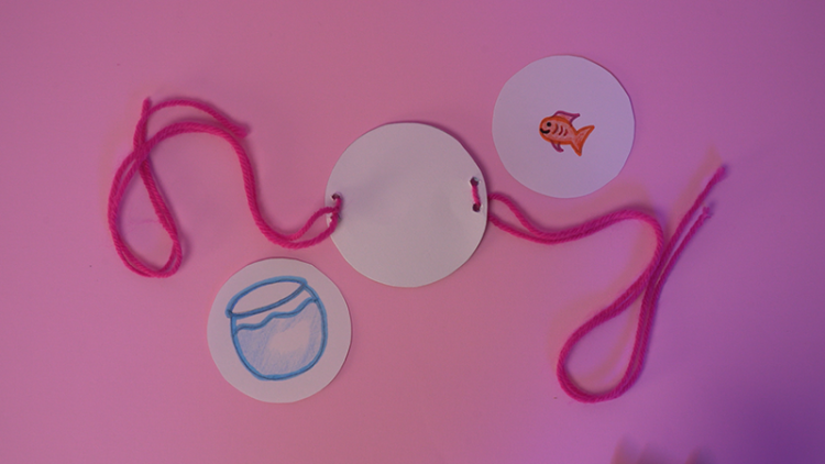 Three circles on a table, one has string threaded on either side, one has a picture of a fish and the other has a picture of a fish tank