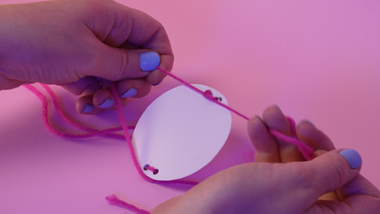 Two hands thread string through two holes on either side of a cardboard circle