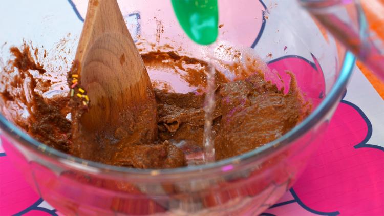 A plastic teaspoon pours water into a runny, brown mixture