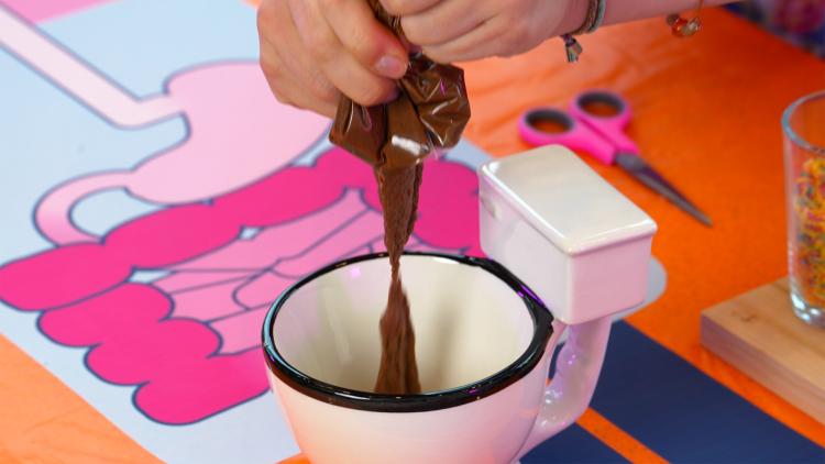 Someone squeezes a sloppy, brown mixture out of plastic sandwich bag and into a toilet-shaped mug