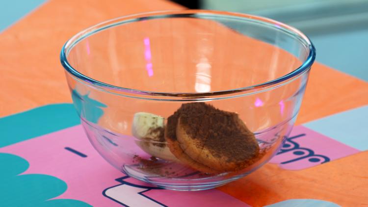 A large glass bowl containing half a banana, three biscuits and some cocoa powder