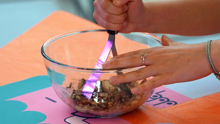 Someone using a kitchen masher to mash up ingredients in a glass bowl