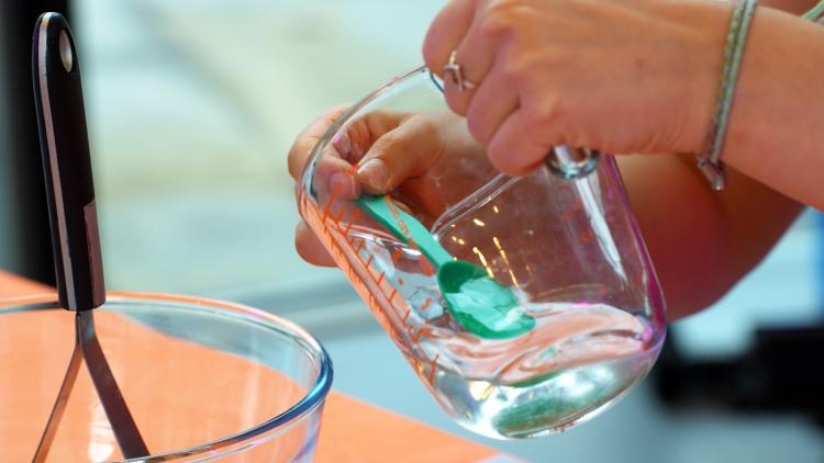 Someone filling a plastic teaspoon with water from a measuring jug