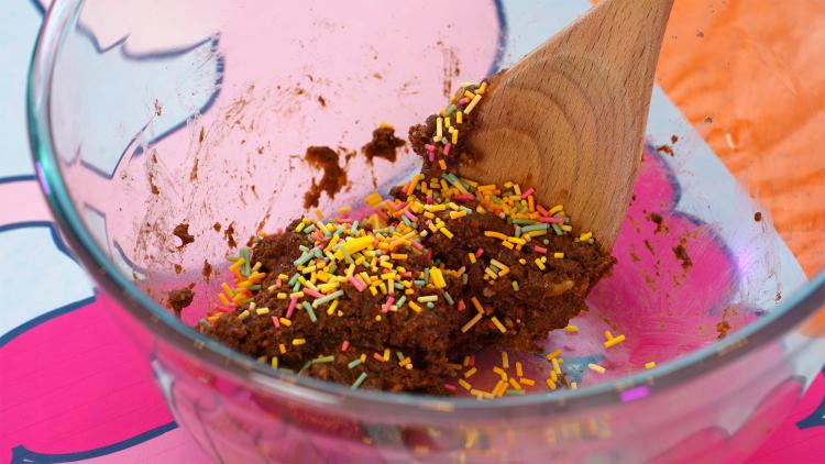 Tiny, multi-coloured sugar sprinkles cover a brown mixture in a glass mixing bowl