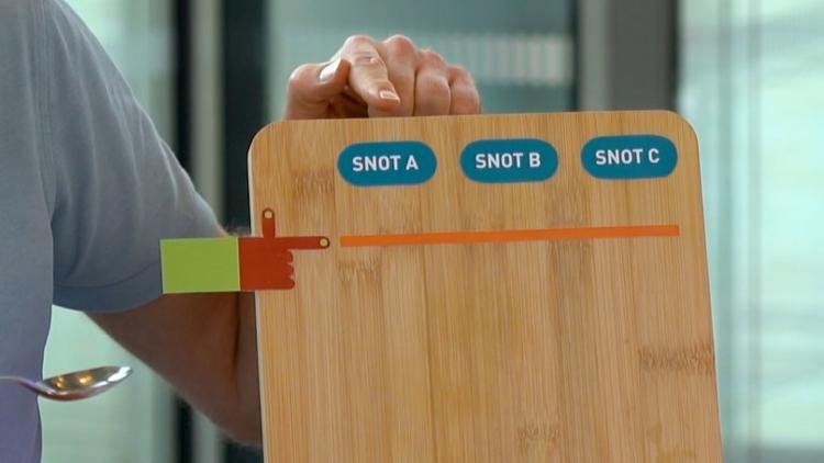 A chopping board propped up vertically, with a race start line and three labels saying 'Snot A', 'Snot B' and 'Snot C'.