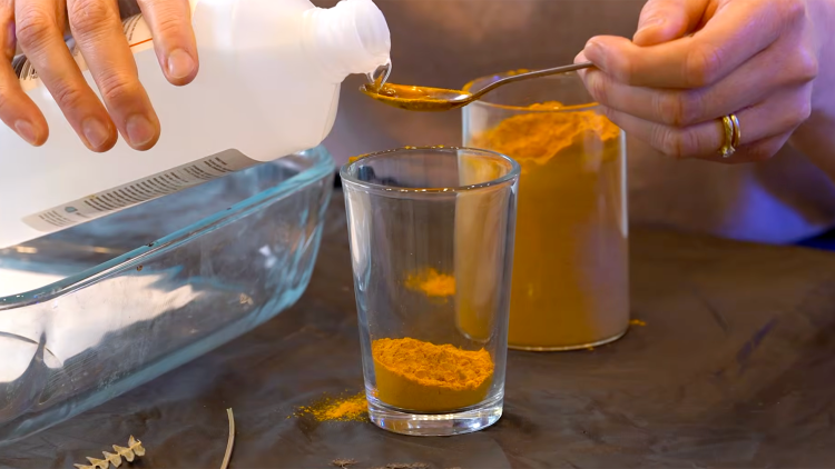 Someone mixing surgical spirit with turmeric in a glass - they are using a spoon to measure in the spirit