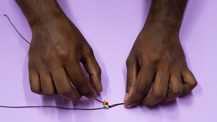 Two hands threading beads onto black elastic