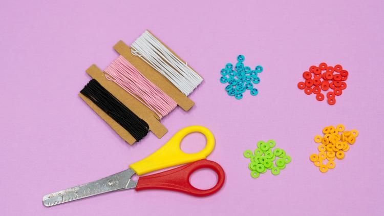 Some scissors, beads and elastic against a pink backdrop