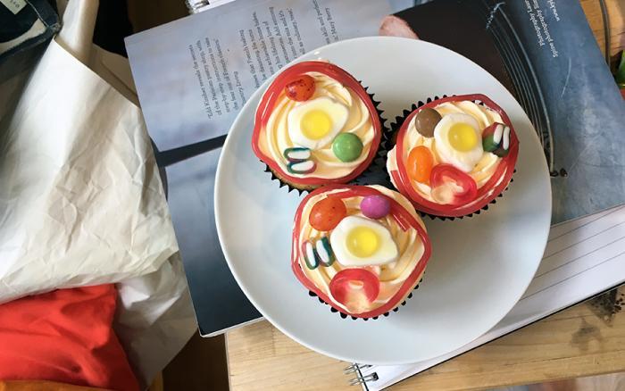 Three cupcakes with different sweets on them sitting on a plate.